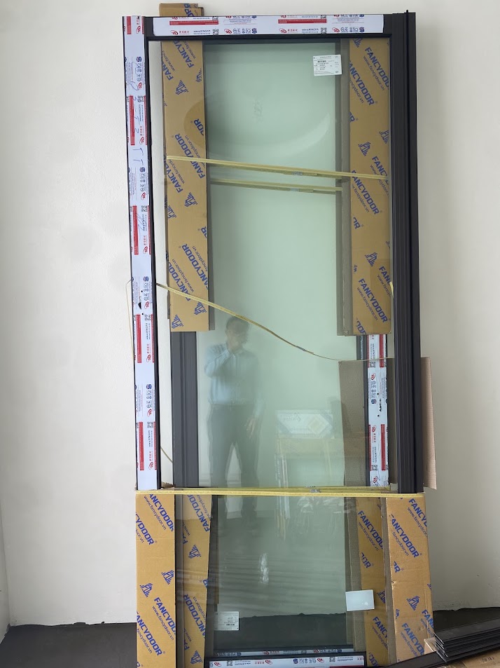 Cửa kính khung nhôm FAMIDOOR mới, còn bọc bảo vệ, dựng sát tường chờ lắp đặt